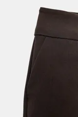 Bermudas de tiro medio y cintura ancha, color marrón, con bolsillos delanteros y cierre frontal con cremallera y ganchos metálicos.