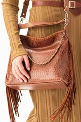 Cartera tipo bandolera color tabaco con textura de cuero grabado croco. Presenta flecos laterales largos, una cadena decorativa frontal y correas ajustables. El diseño combina cuero grabado con detalles de cuero liso y herrajes metálicos.