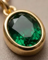 Collar de cadena fina dorada con dije ovalado de piedra verde esmeralda en marco de bronce.