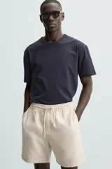 Bermuda de algodón color beige claro, de corte regular fit, con cintura elástica ajustable mediante cordón. Presenta bolsillos laterales y un bolsillo trasero de vivo.