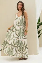 Vestido largo de tirantes en color blanco con estampado botánico en tonos verde y marrón, escote redondo y falda con volados en el ruedo.