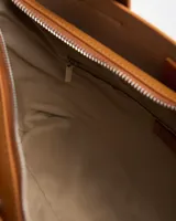 Cartera tipo tote de símil cuero color habano, con asas de mano fijas, detalles de tiras verticales decorativas y correa ajustable removible. Cuenta con el logo metálico de la marca en el frente.