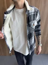 Chaqueta de paño a cuadros en tonos blanco, gris y negro, con forro interior de corderito sintético blanco, cuello clásico, cierre frontal con botones y bolsillo en el pecho.