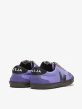 Zapatillas Veja modelo Volley, color lila con logo lateral en negro, detalles en cuero negro en el talón y cordones color naranja. Fabricadas con cuero y gamuza. Inspiradas en las zapatillas de voleibol brasileñas de los años 70.