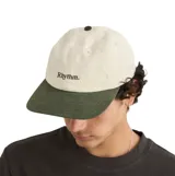 Gorra tipo baseball de diseño bicolor, con cuerpo en color beige y visera en color verde oscuro. Presenta el logo de la marca Rhythm bordado en el frente en color verde y botón superior a tono con la visera.