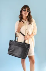 Cartera tipo tote de cuero graneado negro, con diseño clásico y textura uniforme. Cuenta con doble asa de hombro, bolsillo frontal con cierre magnético, bolsillo trasero con cierre metálico y compartimento principal con cierre. El interior está forrado y dispone de múltiples bolsillos organizadores.