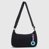 Cartera tipo baguette de Bubba, confeccionada en material con textura similar al gamuzado en color negro. Presenta una correa ajustable con logo grabado, cierre superior y un charm decorativo compuesto por un cordón violeta y una pieza circular turquesa con el logo de la marca.