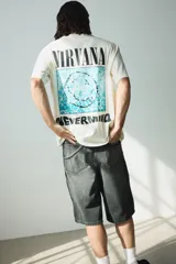 Remera color crema de corte holgado con estampado frontal del logo de la banda Nirvana y el título de su álbum Nevermind en color negro.