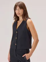 Chaleco negro sin mangas, de corte recto y largo a la cintura, con cuello redondo y cierre frontal oculto.