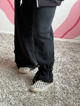 Pantalón de tela deportiva con felpa en color negro, de corte holgado y diseño con presillas en los tobillos para ajustar con lazo.