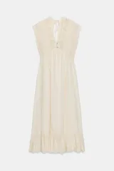 Vestido largo color crudo, sin mangas, con escote en V pronunciado, canesú superior de tejido de punto con botones frontales y lazo para atar en el cuello, y falda fluida con detalle de bordado en el bajo.