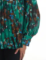 Blusa de gasa plisada con estampado abstracto en tonos verdes, azules y marrones. Presenta cuello alto, mangas largas abullonadas con puños abotonados y un corte holgado con caída fluida.