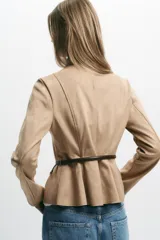 Chaqueta color beige con efecto ante, cuello redondo, manga larga y cierre frontal con cremallera. Presenta un bajo en evasé y un cinturón fino de cuero marrón oscuro con hebilla metálica.