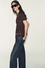 Camiseta de manga corta y cuello redondo, color marrón oscuro, con apliques de perlas de diferentes tamaños distribuidos en el escote y el bajo.