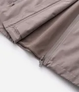 Campera rompevientos de color gris oscuro, con capucha ajustable mediante cordones, cierre frontal por cremallera y bolsillos laterales con cierre. Presenta puños elásticos y un diseño liso y minimalista.