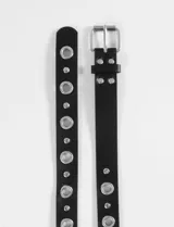 Cinturón negro de cuero sintético con hebilla metálica plateada, ojalillos y tachas plateadas.