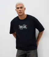 Remera de corte boxy en color negro, con cuello redondo y mangas cortas. Presenta un estampado gráfico en la espalda que muestra a los personajes Joker y Harley Quinn con la frase 'Mad Love'.
