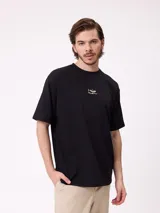 Remera negra de corte holgado con pequeño logo bordado en el pecho que incluye un diseño de pez y la marca Rusty.