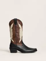 Bota texana de cuero bicolor, combinando el color negro en la base y el marrón en la caña. Presenta un diseño de apliques decorativos en color beige con forma de alas a los costados y taco cuadrado de 5 cm.