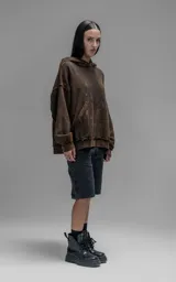 Hoodie de corte oversize y largo crop, confeccionado en algodón con efecto de desgaste y color óxido. Presenta costuras expuestas, detalles de roturas en los bordes y bolsillo frontal tipo canguro.