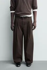 Pantalón chino de corte wide fit confeccionado en tejido de algodón. Presenta pliegues frontales, bolsillos laterales y bolsillos traseros de vivo, con cierre frontal de cremallera y botón.