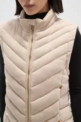 Chaleco acolchado de diseño capitoneado con cierre frontal y bolsillos laterales. Presenta un cuello alto y detalles de botones metálicos decorativos.