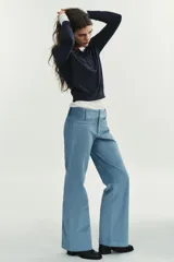 Pantalón de tiro alto con corte flare, confeccionado en pana. Presenta cintura ancha con trabillas, falsos bolsillos delanteros y cierre frontal con cremallera, botón oculto y ganchos metálicos.