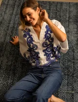 Blusa blanca de algodón con bordados azules, escote en V, cierre frontal con botones y mangas 3/4 dolman.