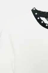 Camiseta blanca de manga corta y cuello redondo, con ribete negro decorado con perlas blancas en el cuello y los puños.