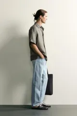 Jeans regular fit de mezclilla negra con efecto lavado, corte recto y tiro medio. Cuenta con diseño de cinco bolsillos y cierre frontal con cremallera y botón.