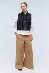 Chaleco de denim azul marino con cuello, bolsillos frontales y bordes festoneados.