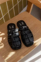 Sandalias bajas de cuero negro con diseño entretejido en el empeine y logo de la marca en la plantilla.