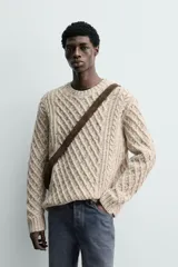 Jersey de punto con diseño de trenzas diagonales, confeccionado en lana con efecto moteado. Presenta cuello redondo, manga larga y terminaciones en rib.