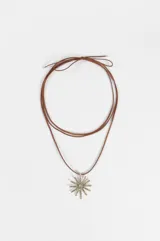 Collar de estilo boho con cordón largo de gamuza color tostado y dije central de metal plateado con forma de sol texturado.