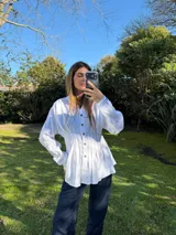 Camisa blanca de silueta entallada con alforzas frontales, cuello clásico, cierre de botones y mangas largas.