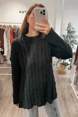 Sweater de punto negro con diseño de trenzas verticales, cuello redondo y corte holgado con aberturas laterales en el ruedo.