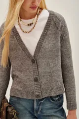 Cardigan de tejido de punto color beige melange, con escote en V y cierre frontal de botones plateados. Presenta mangas largas con puños acanalados.