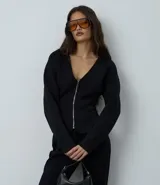 Campera femenina de punto roma en color negro, con diseño acinturado y efecto peplum. Presenta cierre frontal con cremallera metálica, escote en V y bolsillos delanteros.