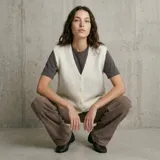 Chaleco de punto color crema con escote en V y cierre frontal con botones. Presenta un diseño sin mangas y corte holgado.