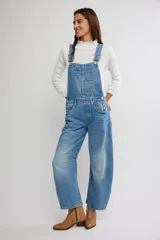 Jardinero enterito de denim en color azul claro, con diseño de peto, tiras regulables y botones laterales. Presenta corte amplio estilo barrel con piernas abuchonadas y bolsillos frontales.