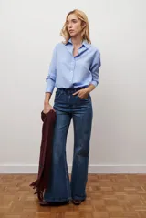 Camisa de mujer a rayas verticales blancas y rosadas, con cuello clásico, cierre de botones frontal y mangas largas con puños abotonados.