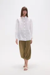 Camisa de algodón color blanco, de corte holgado y manga larga. Presenta detalles de encaje tipo puntilla en el frente, espalda y mangas, con cierre frontal de botones y cuello camisero clásico.