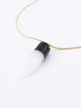 Cadena fina de color dorado con un dije colgante compuesto por una pieza superior negra y una piedra blanca en forma de colmillo.
