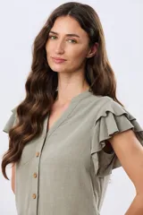 Camisa de lino y viscosa color beige, con cuello mao, escote en V y botones frontales de madera. Presenta mangas cortas con volados delicados.