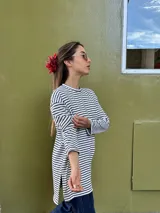 Remerón de manga larga con diseño de rayas horizontales finas en color negro sobre fondo blanco. Presenta un corte oversize, cuello redondo y un largo asimétrico con la parte trasera ligeramente más larga que la delantera.