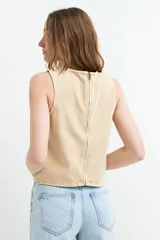 Top de denim sin mangas, color crudo, con cuello redondo y costura central visible.