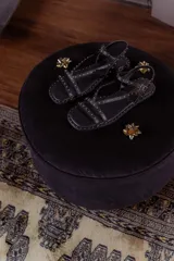 Sandalias planas de cuero negro con múltiples tiras finas adornadas con tachas doradas. Cuentan con cierre de hebilla en el tobillo.