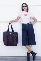 Bolso tipo tote de diseño urbano, confeccionado en material impermeable acolchado de color negro. Cuenta con doble asa de hombro, compartimento principal con cierre, bolsillo frontal con cierre y detalle de logo circular en la parte superior.