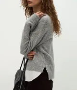 Suéter de punto jaspeado en color gris oscuro, con cuello redondo y mangas largas. Presenta un diseño integrado con una camisa blanca debajo, creando un efecto de capas superpuestas.
