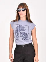 Remera de manga corta color lila claro, con cuello redondo y bordes deshilachados. Presenta un estampado central de dos leopardos dentro de un marco cuadrado, con los patrones de sus manchas en forma de corazones.